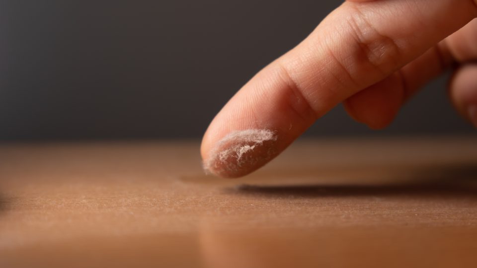Touching the dust on a surface of furniture with finger