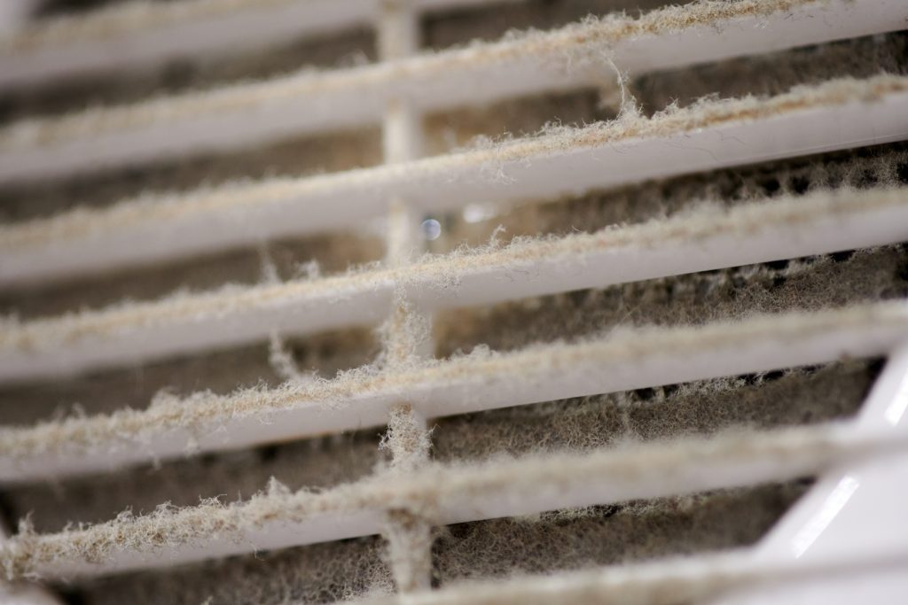 Close-up of dusty air vent slats with accumulated lint and fibers along the horizontal louvers.